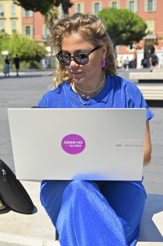 une femme habillée en bleu assise dans la rue avec un ordinateur